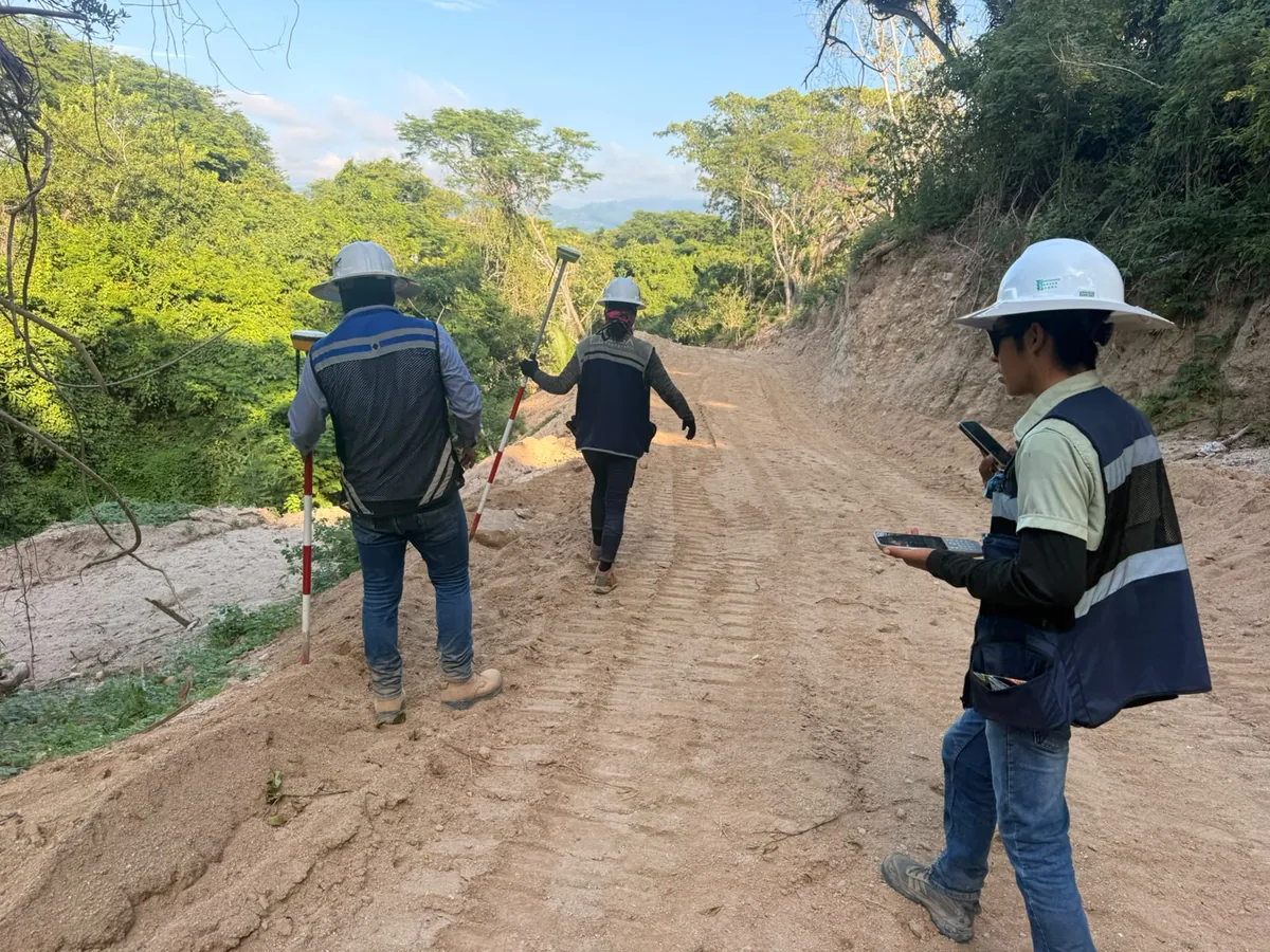 Brigada topográfica de CISA avanzando con bastón y receptor GNSS por un camino de obra
